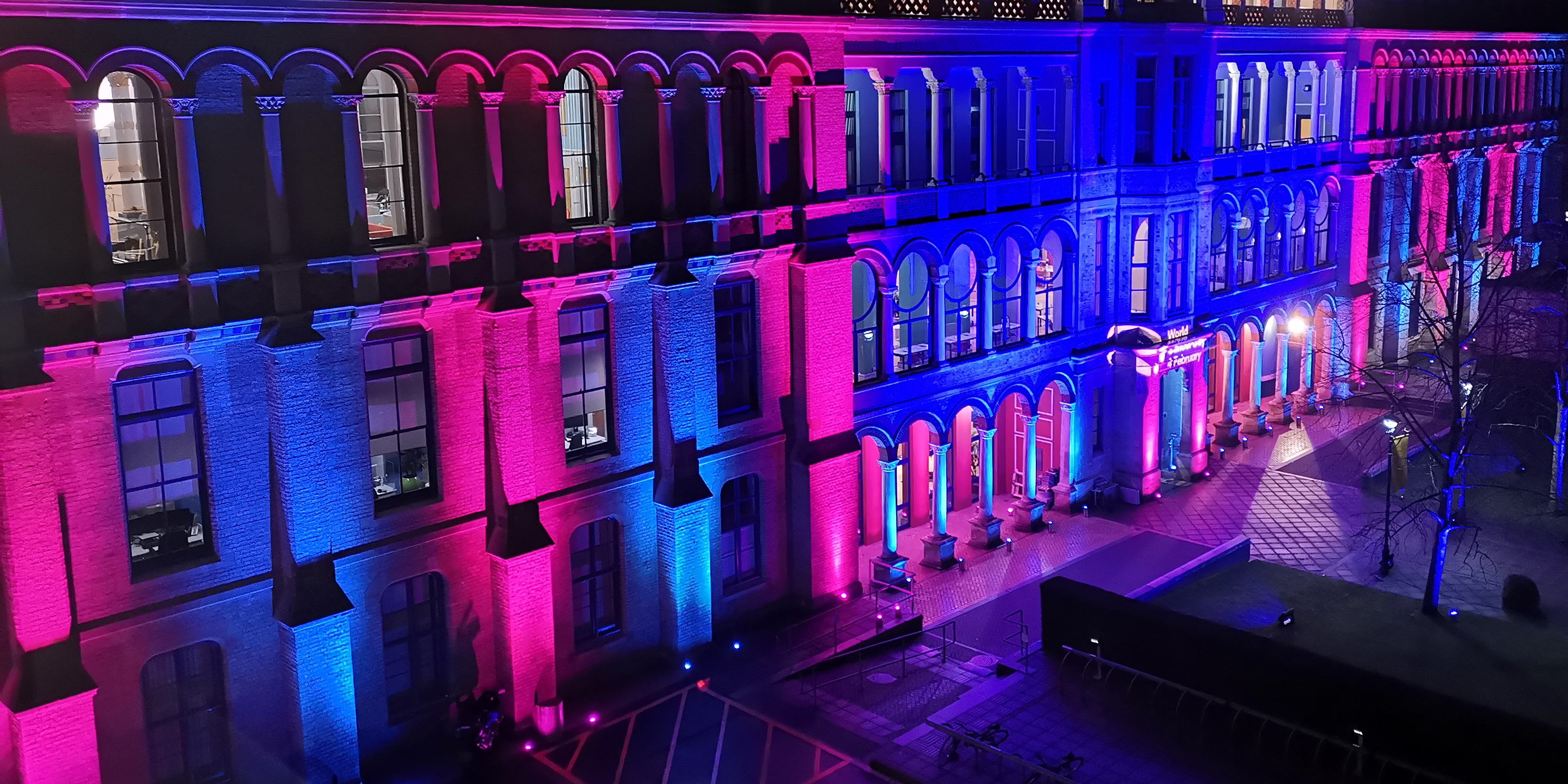 Cambridge Judge Business School from above, illuminated in Cancer Research UK colours